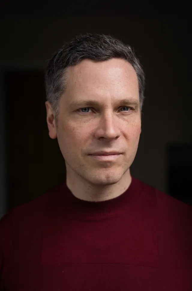 Studio headshot of Allan Radcliffe wearing a maroon turtleneck against a dark background